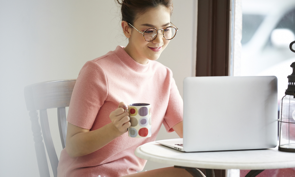 マグカップ片手にノートPCをいじる女性